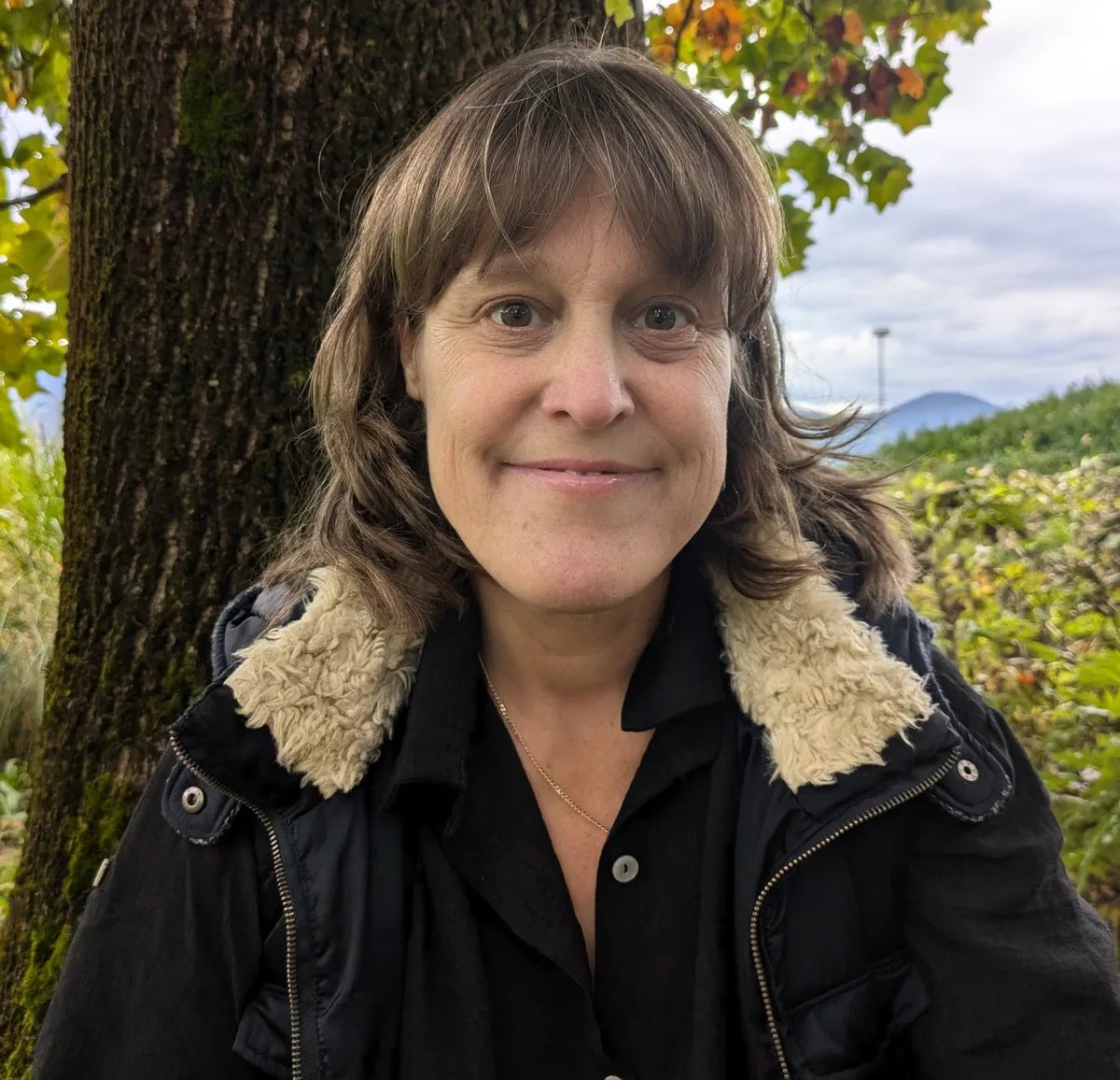 Tania Hauser steht in Winterjacke vor einem Baum und lächelt.